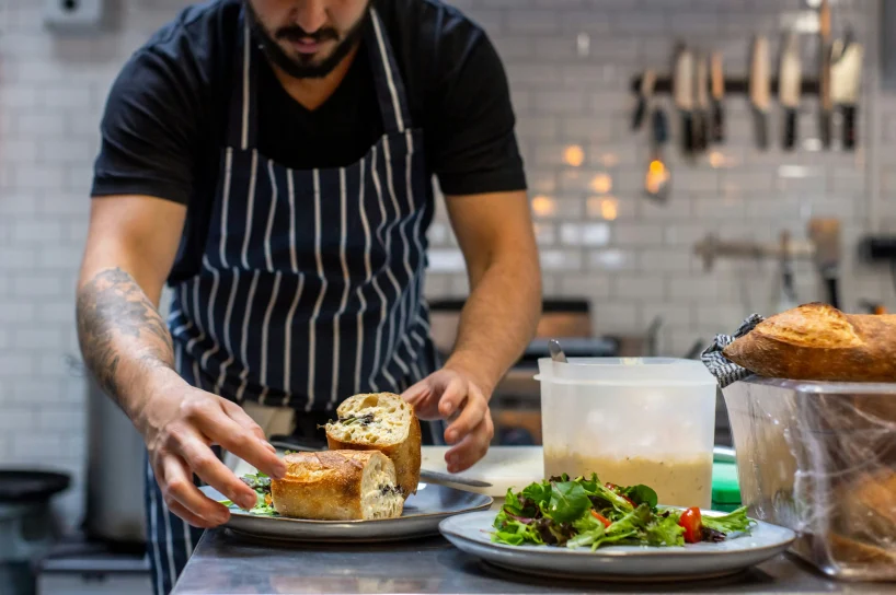 A chef prepares a sandwich on a plate.