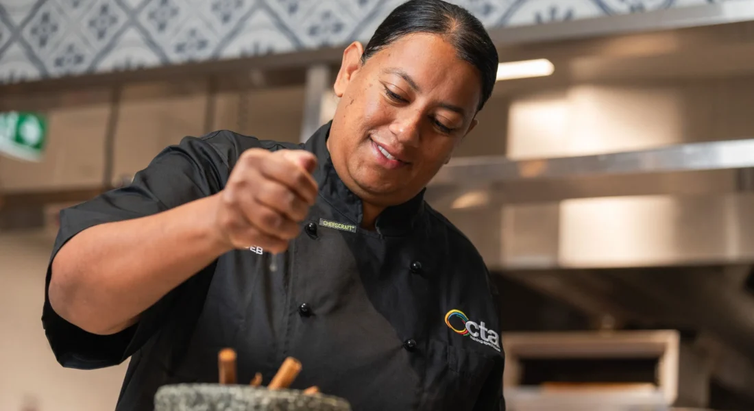 Chef is wearing black jacket and is squeezing lemon into a mortar and pestle filled with spices.