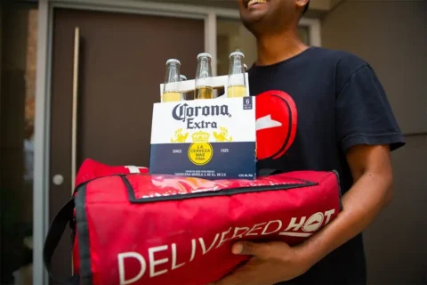 A delivery man carries beers and pizza