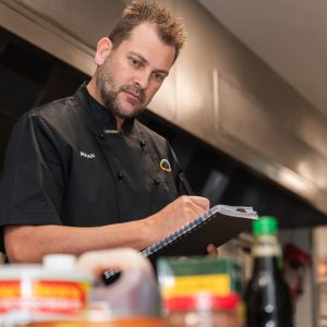 A food safety supervisor writes in a book as he looks at collection of ingredients