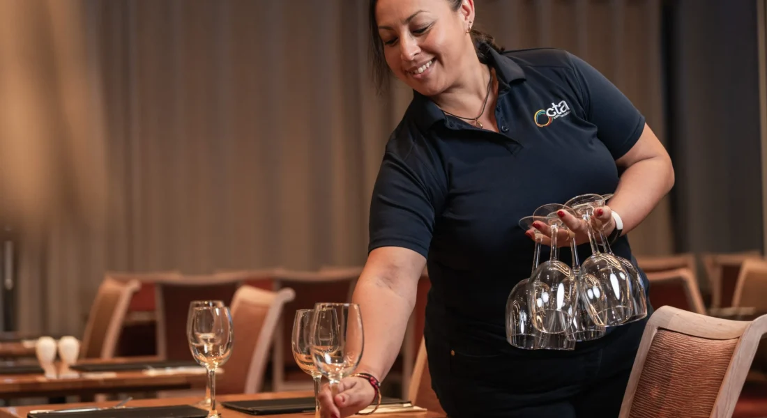 Person places wine glasses on a table while holding other wine glasses.