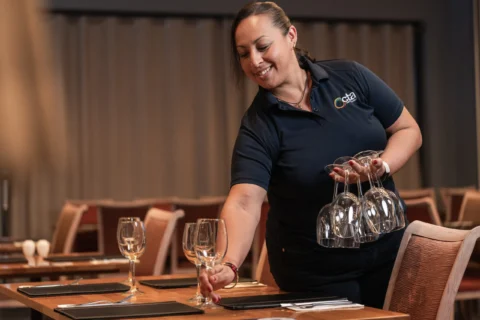 Person places wine glasses on a table while holding other wine glasses.