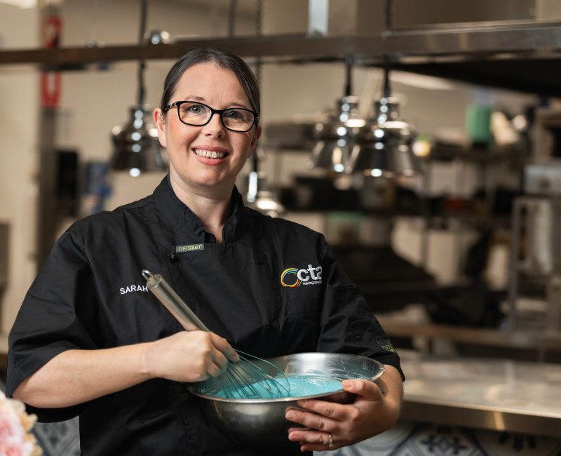 Chef is in a kitchen whisking blue icing in a metal bowl