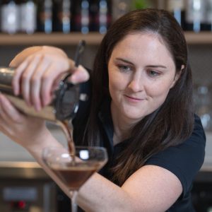 A bartender pours a drink into a tall glass.