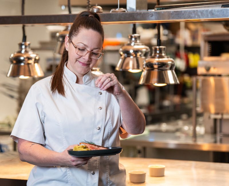 Chef seasons a salmon dish.