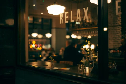 Photo through the front window of a bar at night, there is a sign on the bar window saying relax.