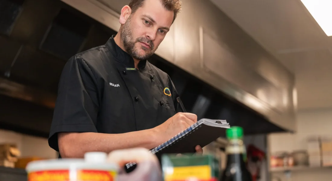 A food safety supervisor writes in a book as he looks at collection of ingredients
