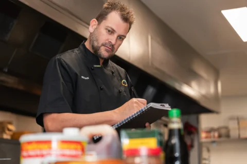 A food safety supervisor writes in a book as he looks at collection of ingredients