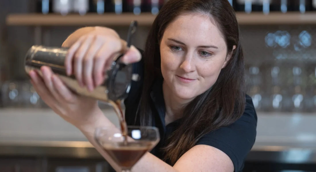 A bartender pours a drink into a tall glass.