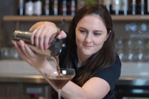 A bartender pours a drink into a tall glass.